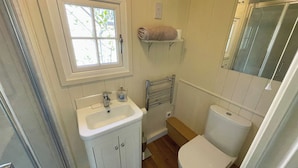 A bathroom with a white sink, a toilet, a window, and a towel rack. - The Shepherds Hut (Wallingford)