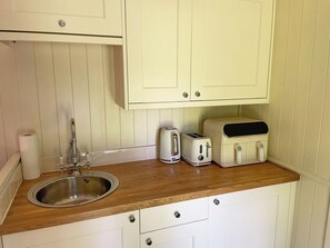 Una pequeña kitchenette con encimera de madera, un lavamanos de acero inoxidable, un tostador y una tetera.