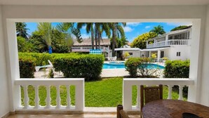 A balcony with a view of a pool, white buildings, and greenery. - Bay City Condos by Linkzup (Sosúa)