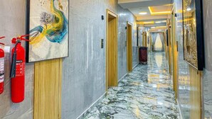 A hotel hallway with marble flooring, artwork on the walls, and a fire extinguisher. - Julicis Hotels and Suites (Lagos)