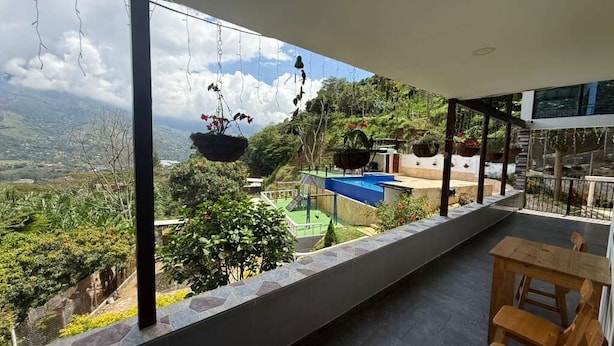 Un balcón con macetas colgantes, un banco de madera y vistas a un paisaje verde.