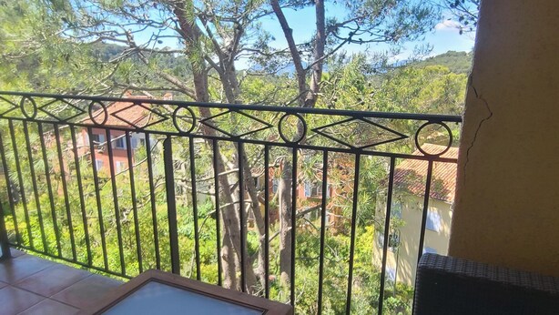 Un balcon avec une balustrade en métal, une chaise en osier et une table en bois.