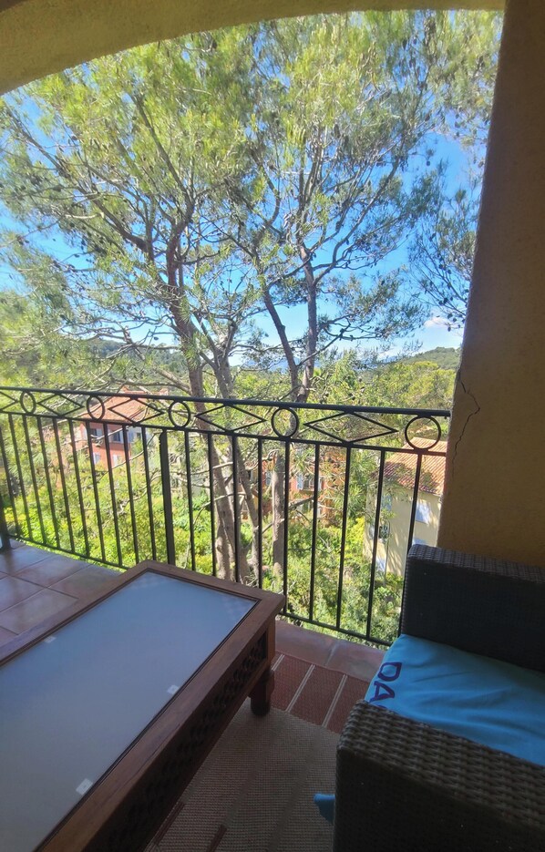 Ein Balkon mit Metallgeländer, einem Korbstuhl und einem Holztisch.