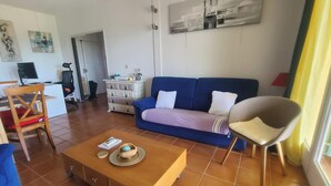 Un salon comprenant un canapé, un fauteuil, une table basse et un bureau avec un ordinateur.