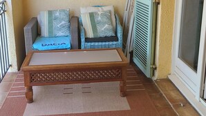 Un balcon avec un banc en bois, deux coussins et un sol carrelé.