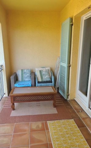 Ein Balkon mit einer hölzernen Bank, zwei Kissen und einem gefliesten Boden.