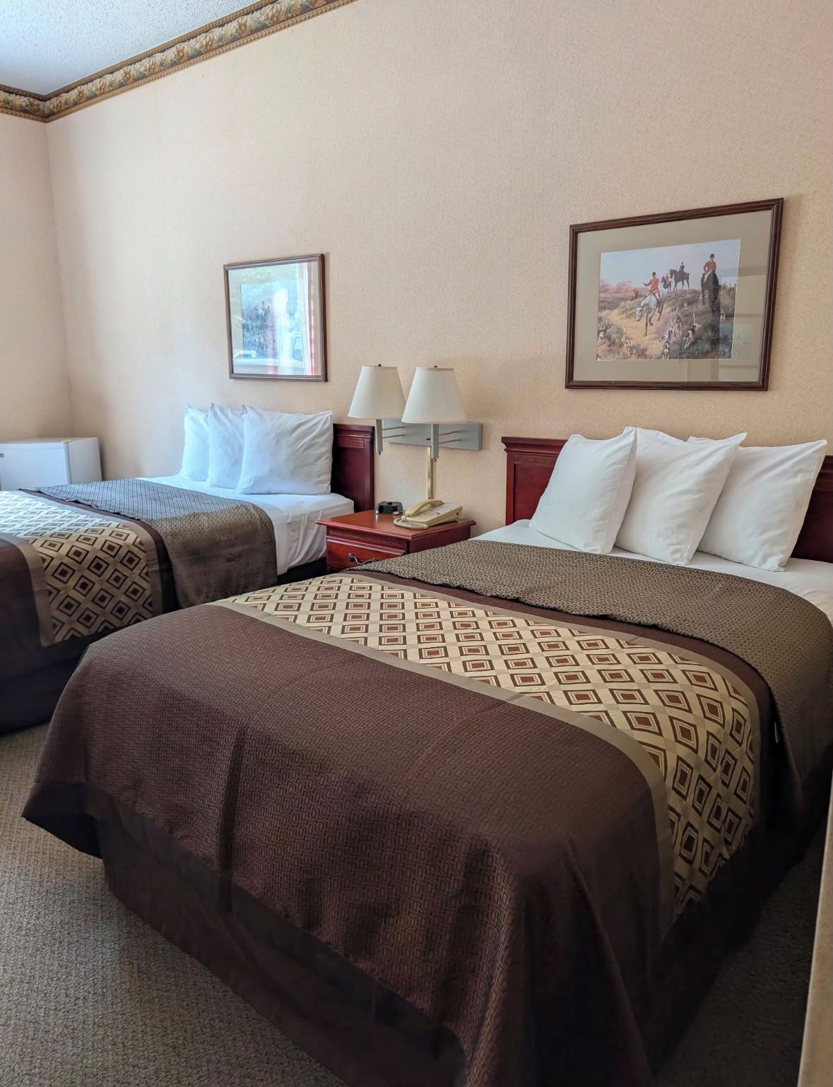 Une chambre d’hôtel avec deux lits, une table de chevet avec une lampe et deux tableaux encadrés au mur.