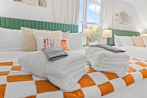 A hotel room with a checkered bedspread, neatly folded towels, and a green upholstered headboard. - New Build | <10 Mins to Folly & <15 to DT (Charleston)