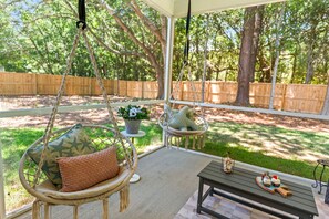 A patio with two hanging chairs, a small table with decorative items, and a view of a fenced yard. - New Build | <10 Mins to Folly & <15 to DT (Charleston)