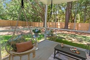 A covered patio area with wicker chairs, a small table, and a hanging swing. - New Build | <10 Mins to Folly & <15 to DT (Charleston)