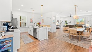 Una cocina amplia con muebles blancos, una isla central y un comedor con mesa y sillas de madera.