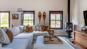 A cozy living room with a sectional sofa, a fireplace, and large windows offering a view of the outdoors.