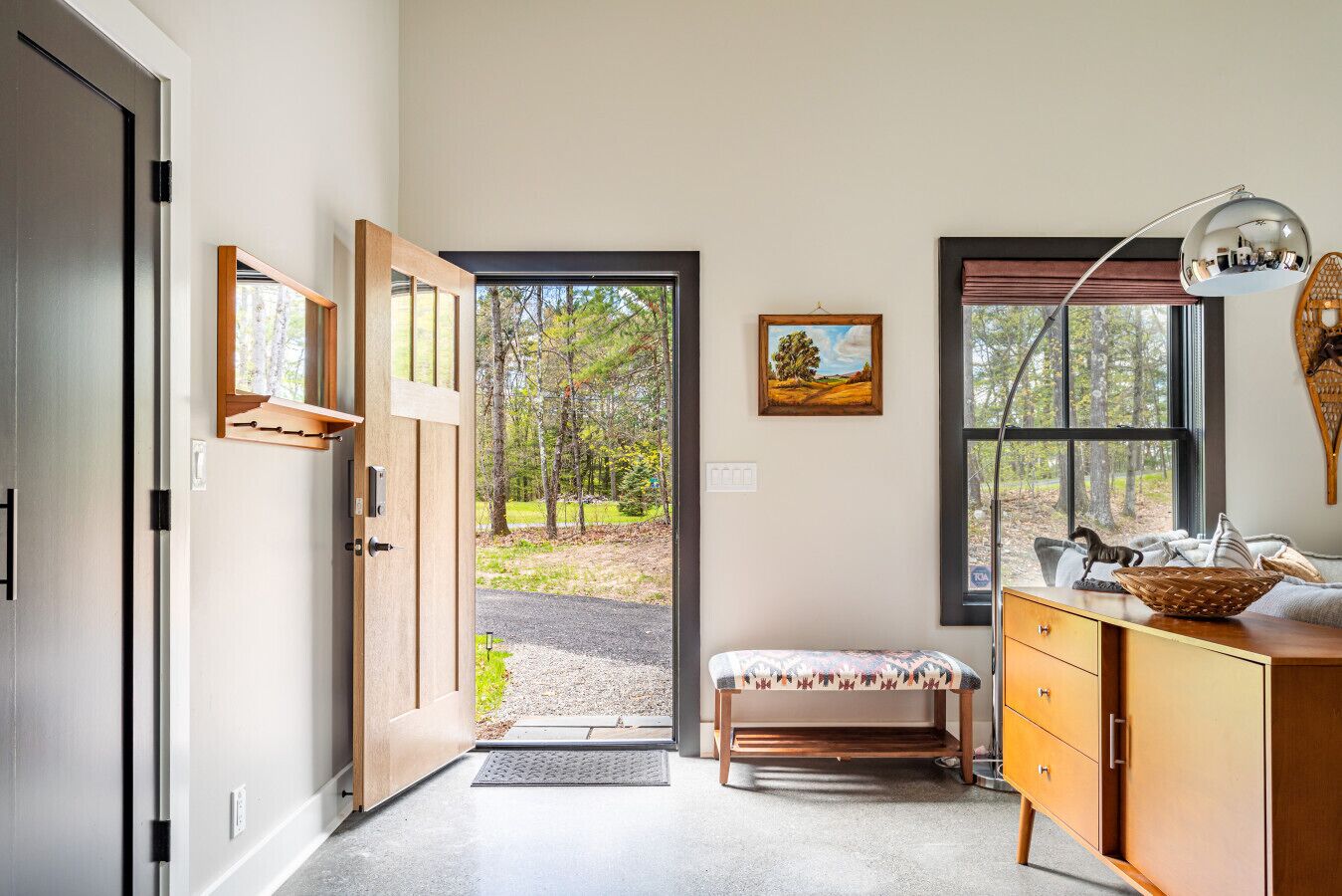 Une pièce avec un banc en bois, un bureau avec une lampe, une porte donnant sur l’extérieur et un tableau encadré accroché au mur.