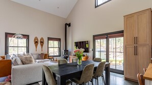 A spacious living area with a sofa, dining table, and chairs, a fireplace, and large windows.
