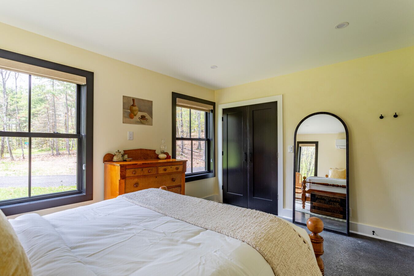 Une chambre à coucher avec un lit, une commode, un miroir et de grandes fenêtres.