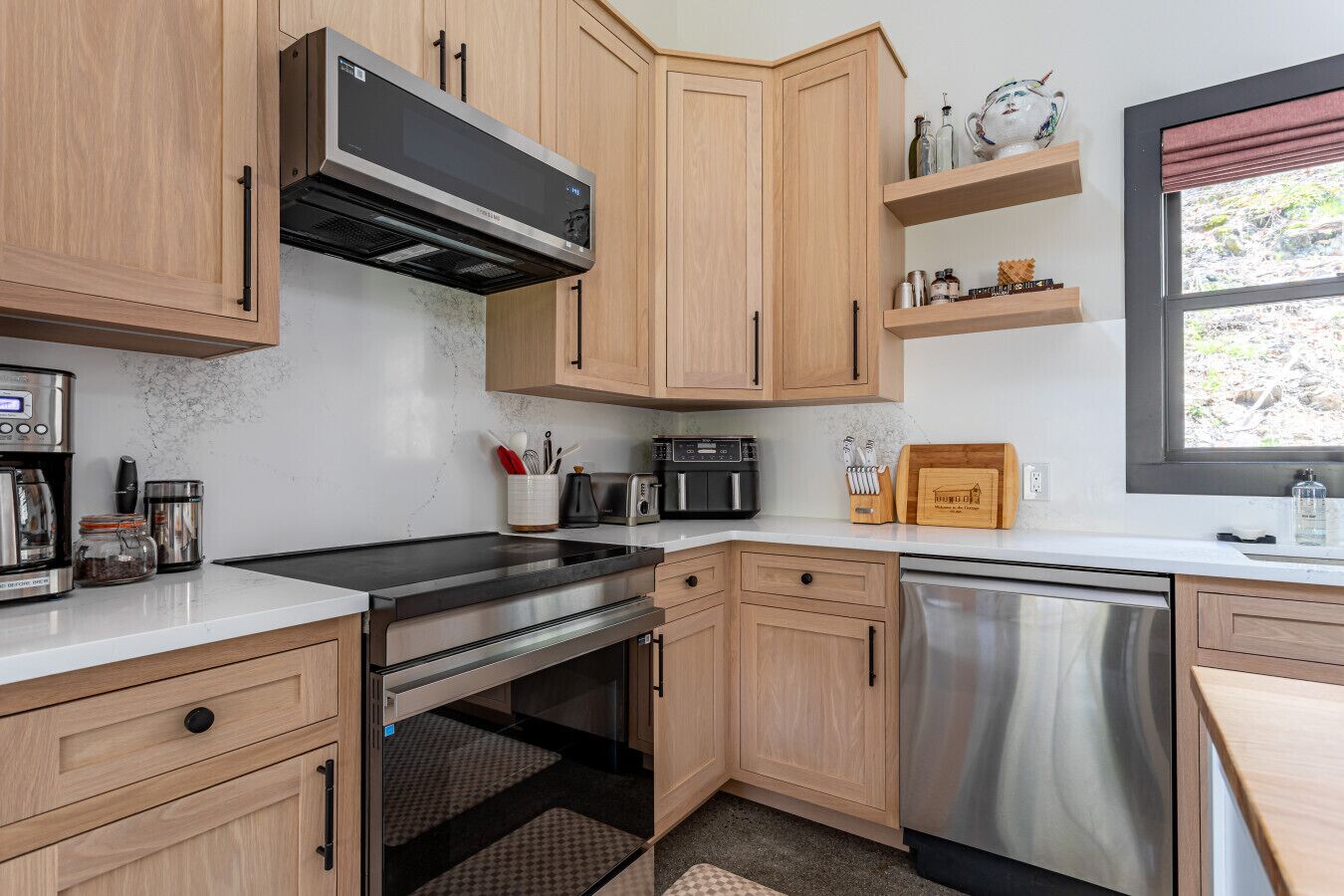 A modern kitchen with wooden cabinets, a built-in oven, a dishwasher, and a window with a view.