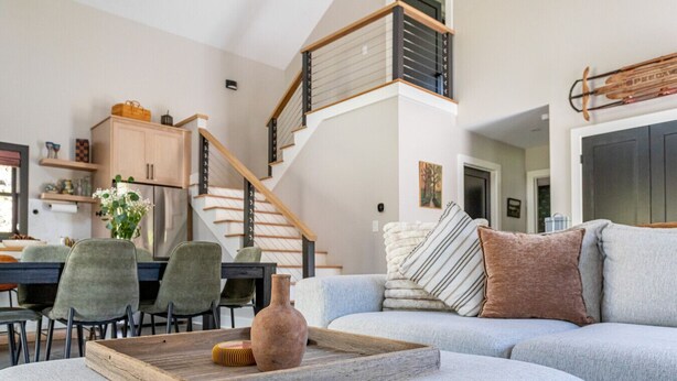 A modern living room with a grey sofa, a wooden coffee table, and a staircase leading to an upper floor.