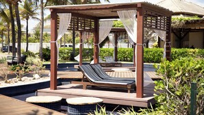 Un pabellón de madera con dos sillones de descanso, una piscina y plantas tropicales.