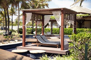 Un pabellón de madera con dos sillones de descanso, una piscina y plantas tropicales.