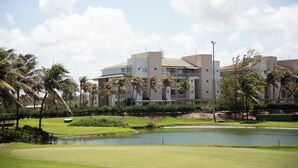 Un campo de golf con un estanque, palmeras y un edificio de varios pisos con balcones.
