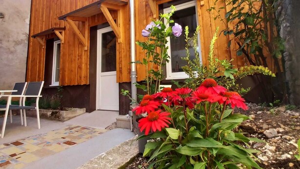 Un edificio de madera con puerta, ventanas y un pequeño jardín con flores rojas.