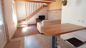 Una habitación amplia con una mesa de comedor de madera, un sofá, un televisor y una escalera que lleva a un nivel superior.