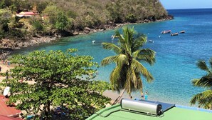 Vista costera con aguas turquesas cristalinas, una playa y una colina con vegetación.