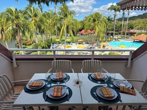A balcony with a table set for four, overlooking a pool area with umbrellas and lounge chairs. - T3 apartment in holiday village - 4/6 persons Sea view & Swimming pool (Rated 3*) (Sainte-Luce)