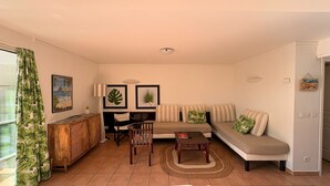 Una sala de estar con sofá, mesa de comedor, sillas, lámpara y decoración de temática tropical.