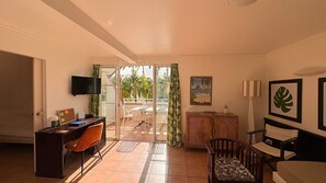 A room with a desk, chair, bed, TV, and a balcony with a view of palm trees. - T3 apartment in holiday village - 4/6 persons Sea view & Swimming pool (Rated 3*) (Sainte-Luce)