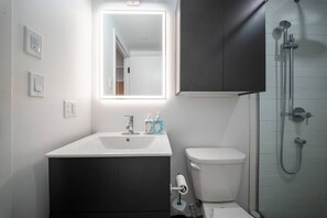 Une salle de bain moderne avec un lavabo blanc, un miroir, des toilettes et une douche.