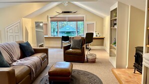 A loft-style living room with a high ceiling, a large window, a fireplace, and a cozy seating area. - Skylights & Tides King Studio - Kittery/Portsmouth (Eliot)