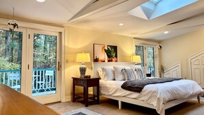 A bedroom with a skylight, a bed, a nightstand, a lamp, and a view of the outdoors. - Skylights & Tides King Studio - Kittery/Portsmouth (Eliot)