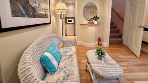 A living room with a sofa, a coffee table, a lamp, a framed picture, a mirror, a small kitchen area, and a staircase. - Skylights & Tides King Studio - Kittery/Portsmouth (Eliot)