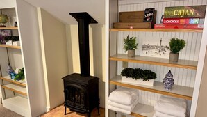 A room with a black wood-burning stove, shelves with board games, and a potted plant. - Skylights & Tides King Studio - Kittery/Portsmouth (Eliot)