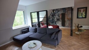 A modern living room with a sectional sofa, a round coffee table, a fireplace, and a large window. - Comfortable Apartment With a Private Sauna (gmina Stężyca)