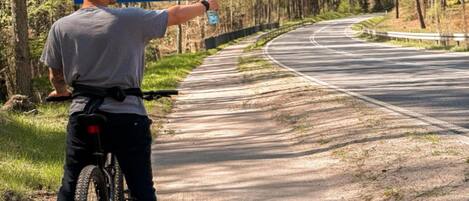 A person pointing at a directional sign on a road surrounded by trees.