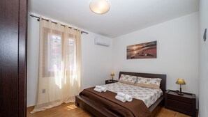 Ein Schlafzimmer mit Bett, Vorhängen, einem Gemälde, einem Nachttisch und einer Klimaanlage.