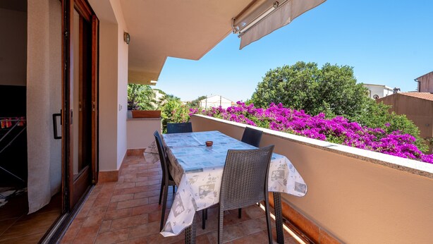 Ein Balkon mit Tisch und Stühlen, Blick zum Himmel und lila Blumen.