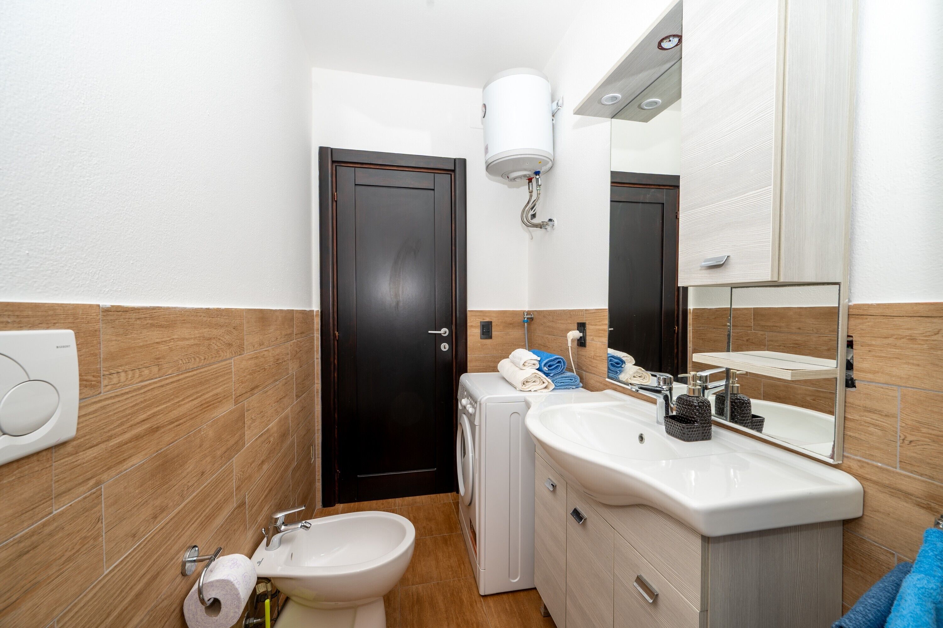 A bathroom with a toilet, sink, mirror, towel rack, and a wall-mounted heater.