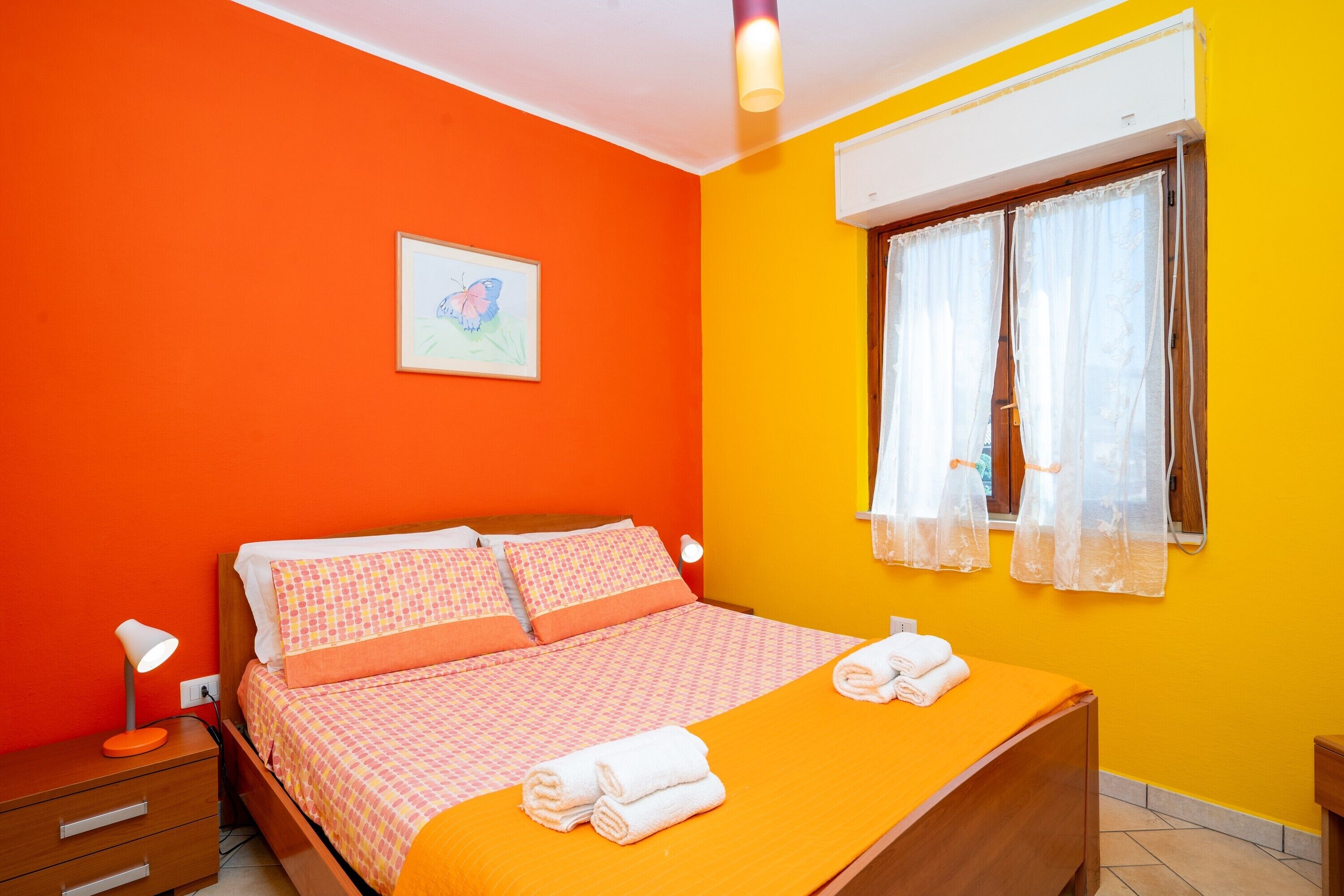 A bedroom with a bed, a nightstand, a window with curtains, and a wall-mounted air conditioner.