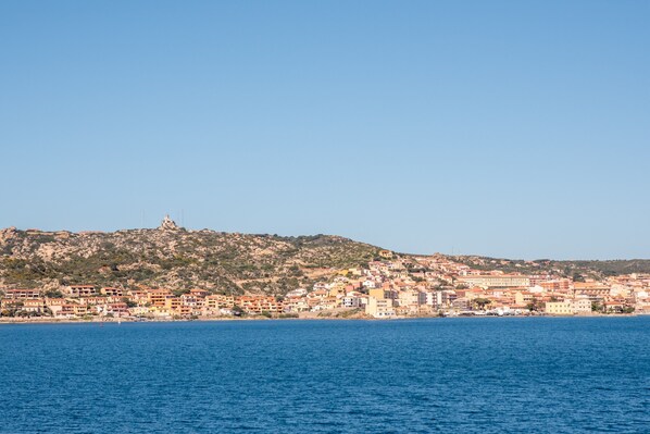 Une ville côtière avec des bâtiments le long du front de mer, une colline surmontée d’une tour et un ciel bleu dégagé.