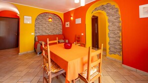A dining area with a table set for four, a sofa, and a door. - Apartment 'Arancio' – Bright 2-Bedroom Retreat in La Maddalena (La Maddalena)