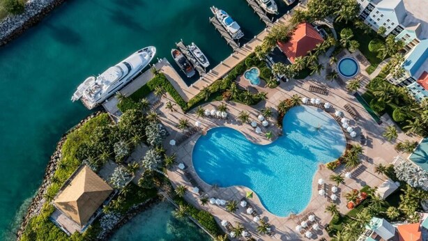 Vista aérea de un resort con una piscina en forma de corazón, un muelle con barcos y un pequeño edificio en forma de pirámide.