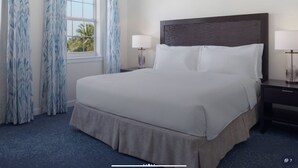 Habitación de hotel con una cama grande, dos mesitas de noche, una ventana con cortinas y vistas a palmeras.