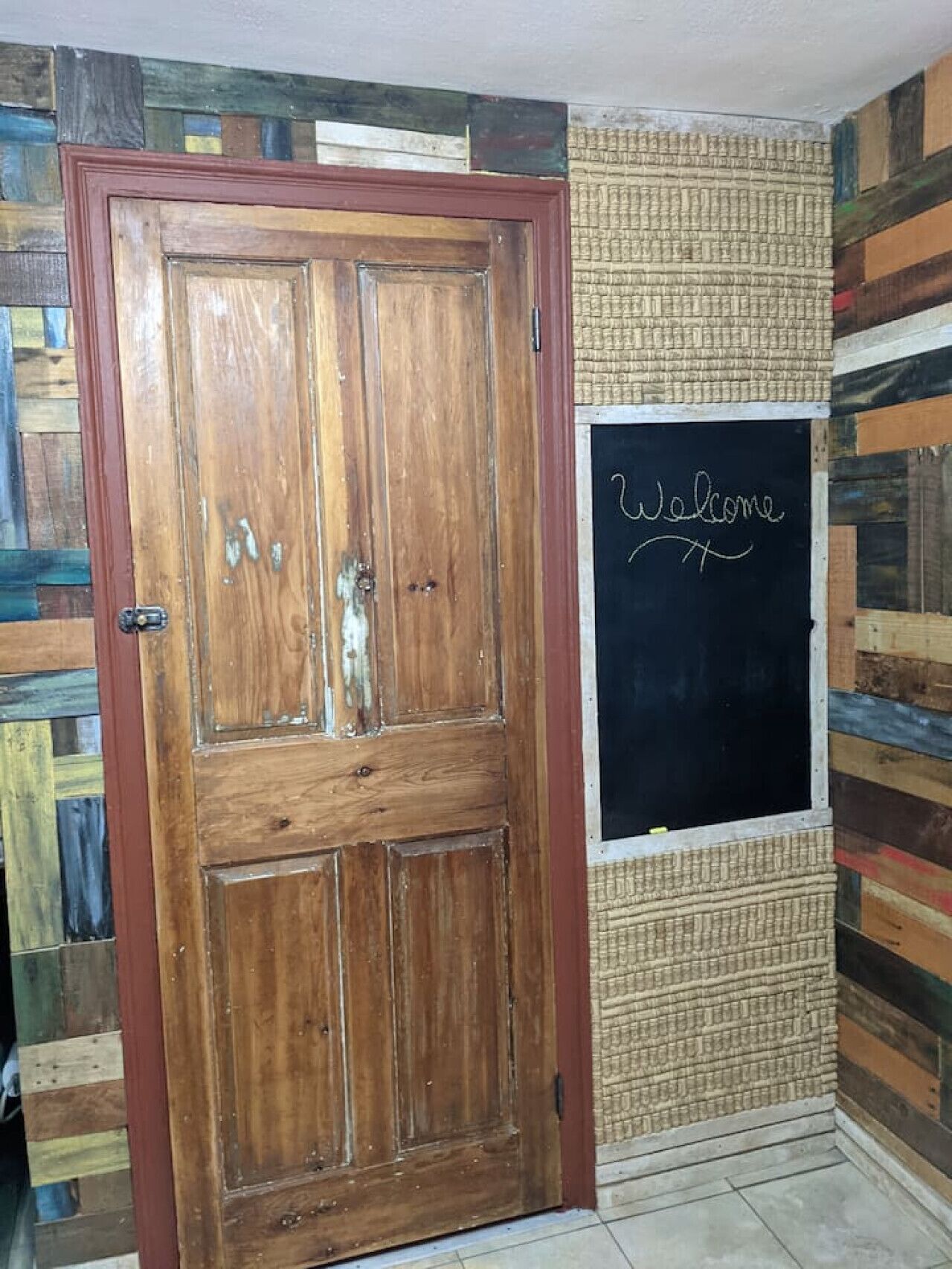 A wooden door with a red frame, a blackboard with 'Welcome' written on it, and a wall with a textured pattern.