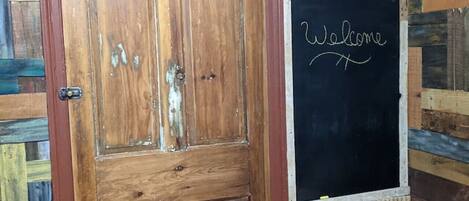 A wooden door with a red frame, a blackboard with 'Welcome' written on it, and a wall with a textured pattern.