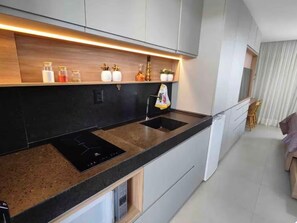 Eine moderne Küche mit schwarzem Arbeitsplatz, zwei Spülen und einem eingebauten Induktionskochfeld. Über dem Arbeitsplatz befinden sich Schränke und links ein kleines Fenster.
