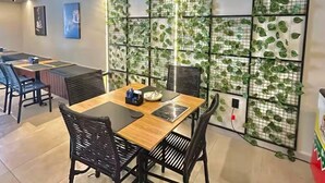 A modern dining area with a wooden table and black chairs, surrounded by walls adorned with green leafy patterns. - Get One 607 · Flat Corais do Bessa with sea view for 4 people (João Pessoa)