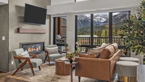 A modern living room with a fireplace, large windows with mountain views, and contemporary furniture. - AlpenPeak Hydeaway at Ascent (Canmore)